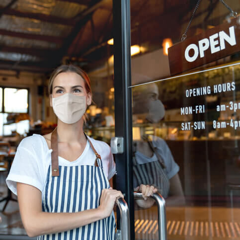 Happy business owner opening the door at a cafe wearing a facemask Happy business owner opening the door at a cafe wearing a facemask to avoid the spread of coronavirus â reopening after COVID-19 concepts