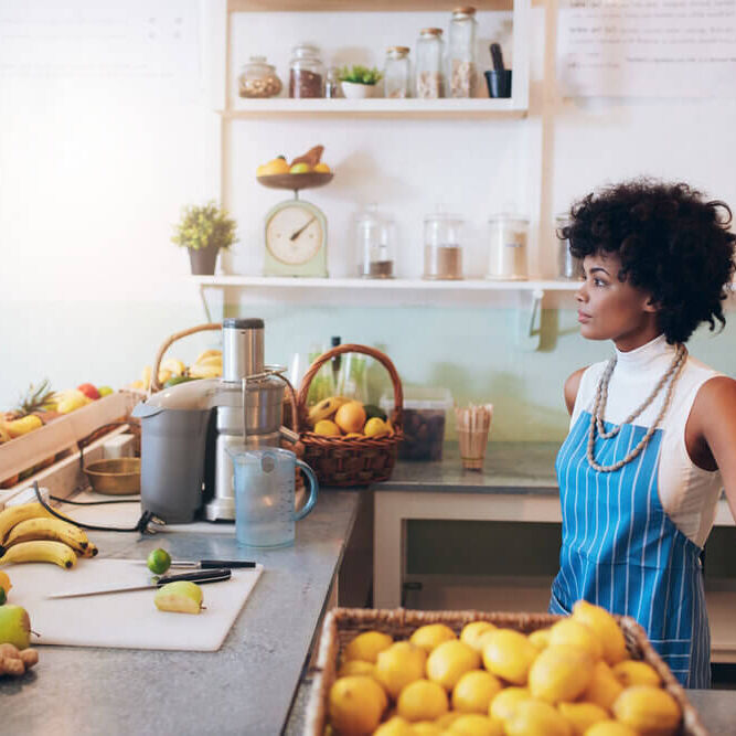 Young female bartender standing at juice bar counter Indoor shot of young female bartender wearing apron standing at juice bar counter looking away and thinking.